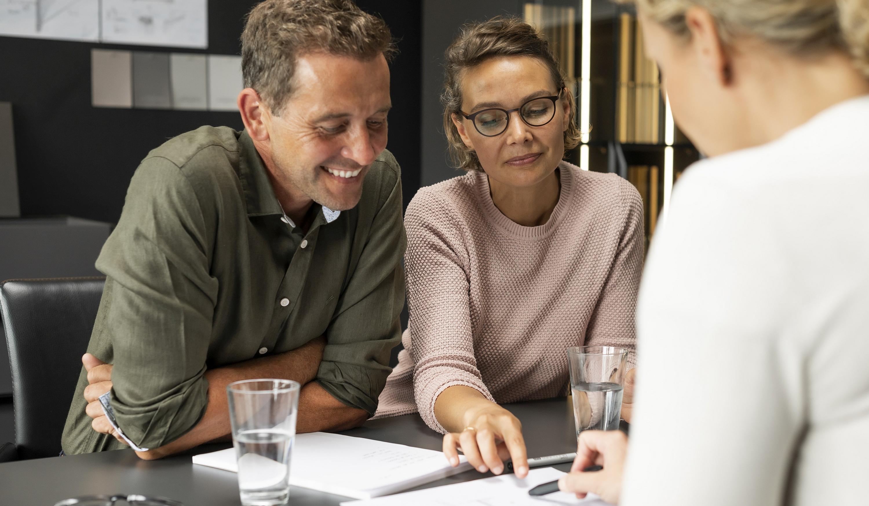 Lachender Mann und neben ihm seine eher kritisch blickende Frau im Küchenstudio bei der Besprechung mit der Küchenplanerin